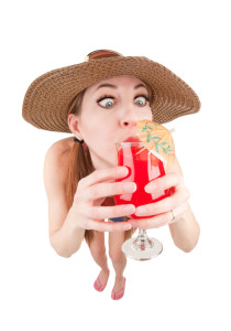 A fisheye image of a woman dressed for a beach vacation guzzling a fancy cocktail.